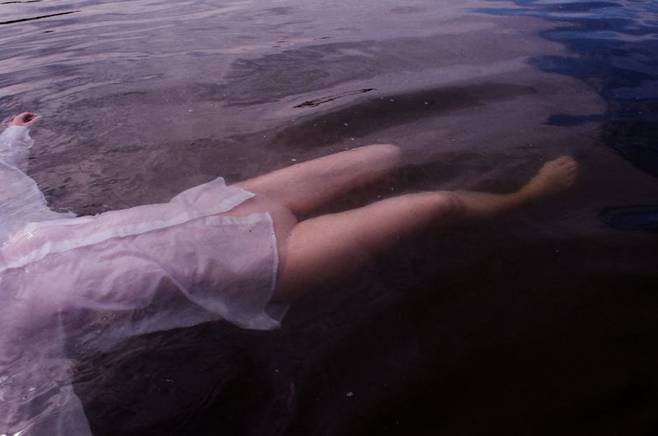 A peaceful scene of a woman floating in a calm body of water, wearing a translucent white shirt.